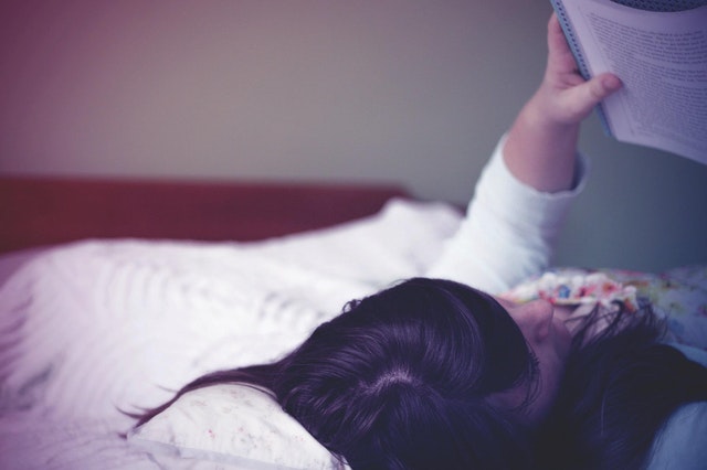 Dievča leží v posteli a číta si knihu.jpg